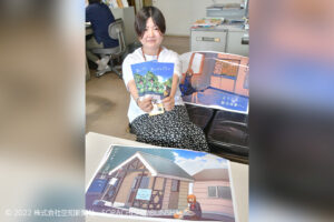 地域おこし作成したイラストを両手に持つ協力隊の岩﨑佳奈美さん