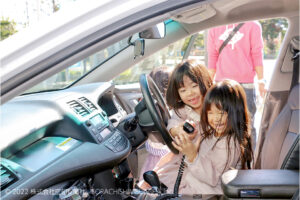 パトカーにのる笑顔の子供たち、運転席のレシーバーを手に持っている